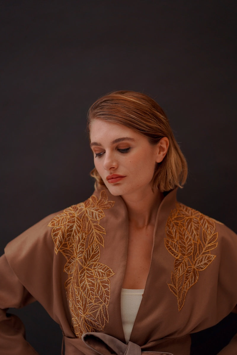 Ecru belted jacket by Nadya Shah featuring a structured design and front pockets, shown on a model in a casual outdoor setting.