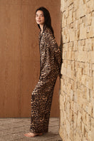 Woman wearing MANITO Jungle Leopard silk pajama set with leopard print, featuring a relaxed fit and silky fabric.