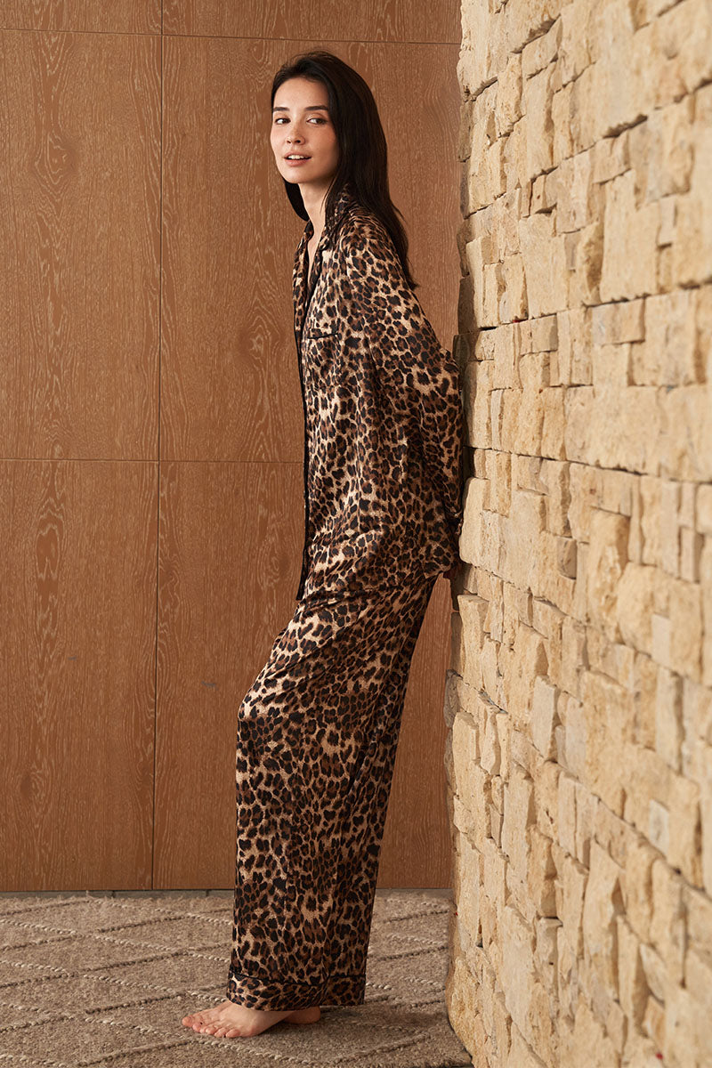 Woman wearing MANITO Jungle Leopard silk pajama set with leopard print, featuring a relaxed fit and silky fabric.