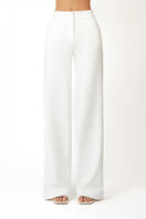 White Khanum's pants with a relaxed fit, shown hanging on a wooden hanger against a neutral background.