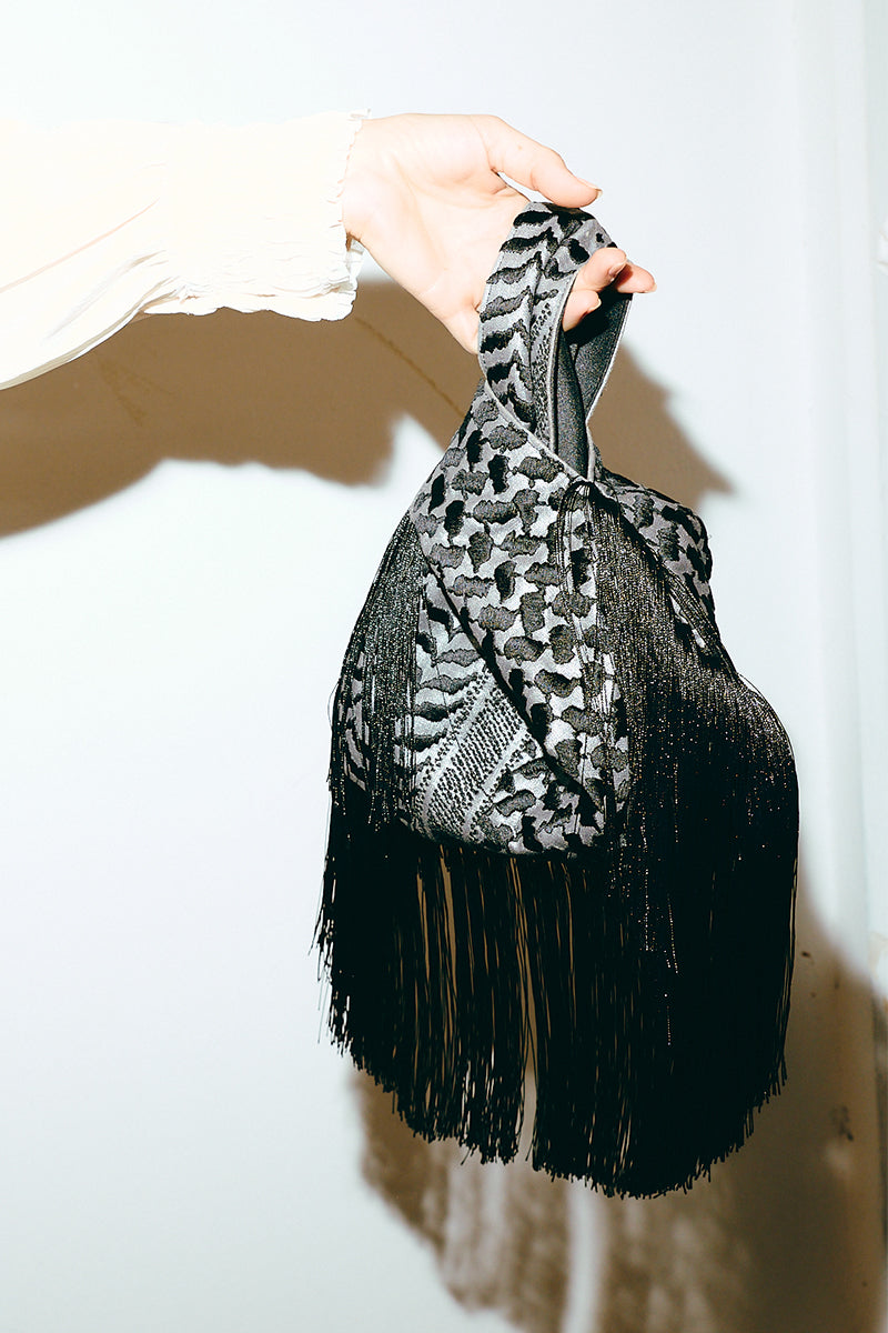 Black keffiyeh slip clutch bag with fringes from Sarah's Bag, featuring a stylish and textured design for everyday or evening use.