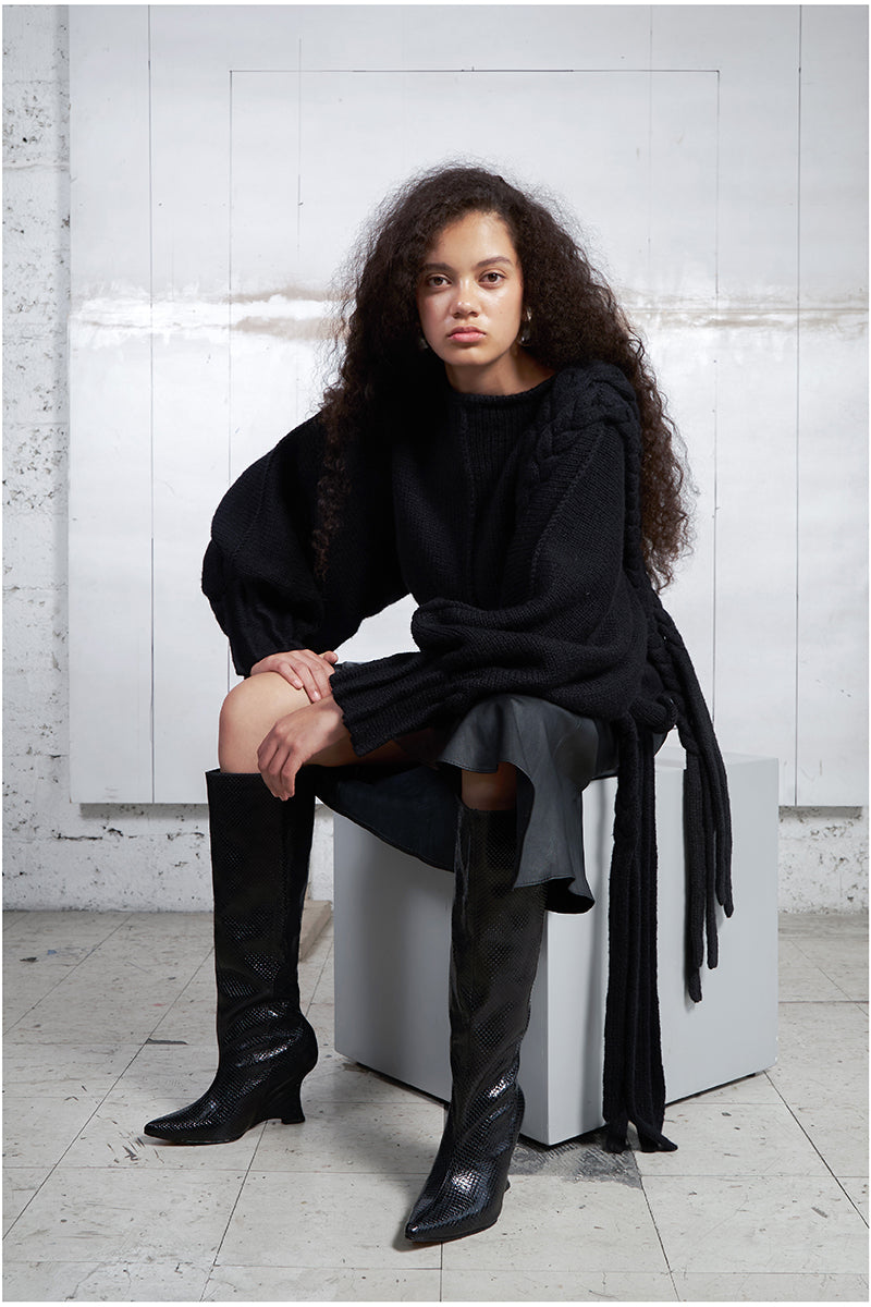 Black knitted sweater with long braids from MAZ Manuela Álvarez, featuring a cozy, textured knit design and long braided details.