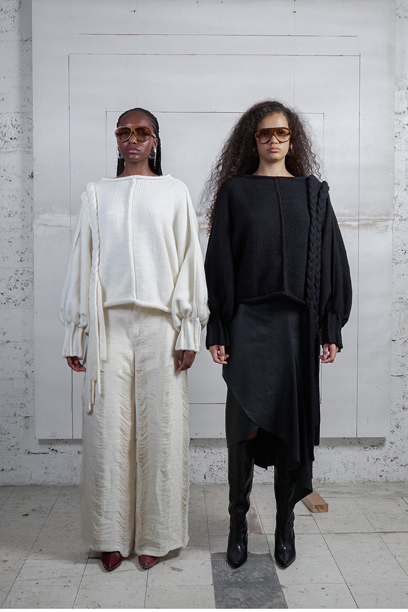 Black knitted sweater with long braid details from MAZ Manuela Álvarez, featuring cozy textured knit and stylish long braid accents.