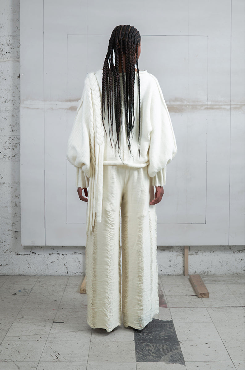 Ivory knitted sweater with long braids by MAZ Manuela Álvarez, featuring a cozy, textured design and long sleeve details.