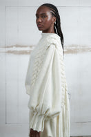 Ivory knitted sweater with long braids by MAZ Manuela Álvarez, featuring cozy knit texture and stylish long braid details.