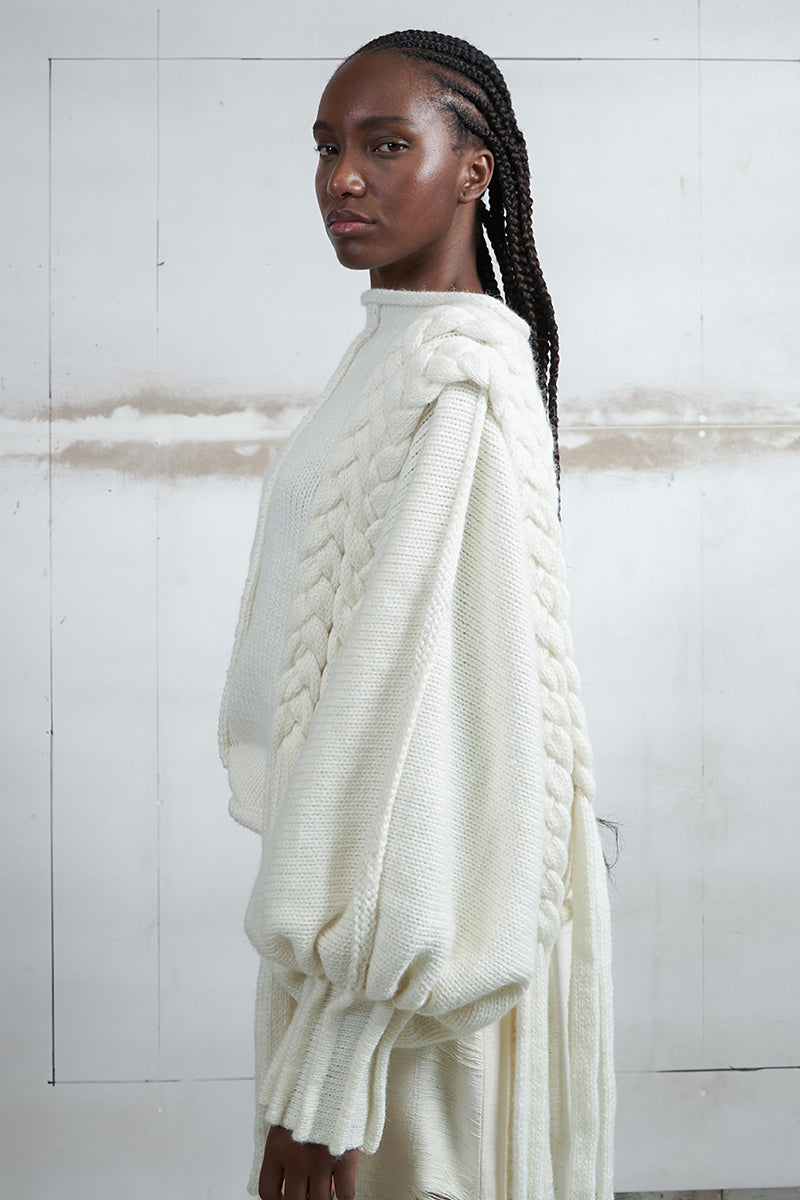 Ivory knitted sweater with long braids by MAZ Manuela Álvarez, featuring cozy knit texture and stylish long braid details.
