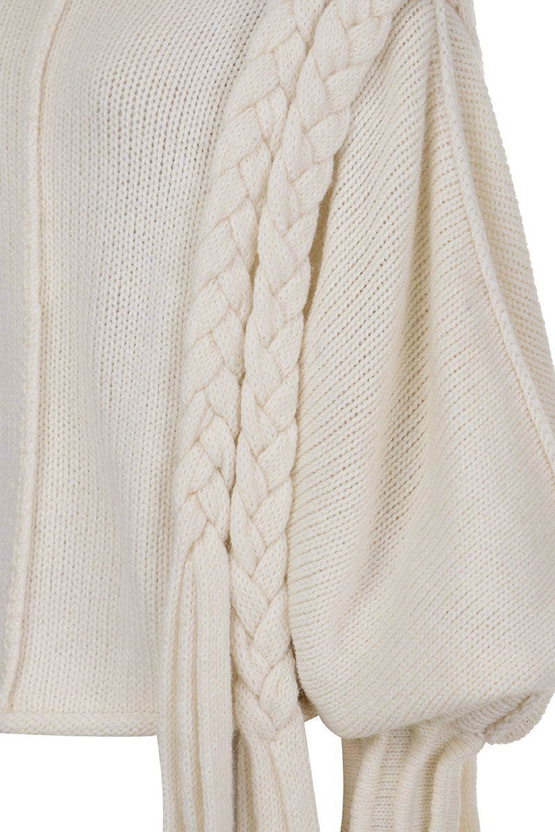 Ivory knitted sweater with long braids by MAZ Manuela Álvarez, featuring cozy, textured knit and long braided details.
