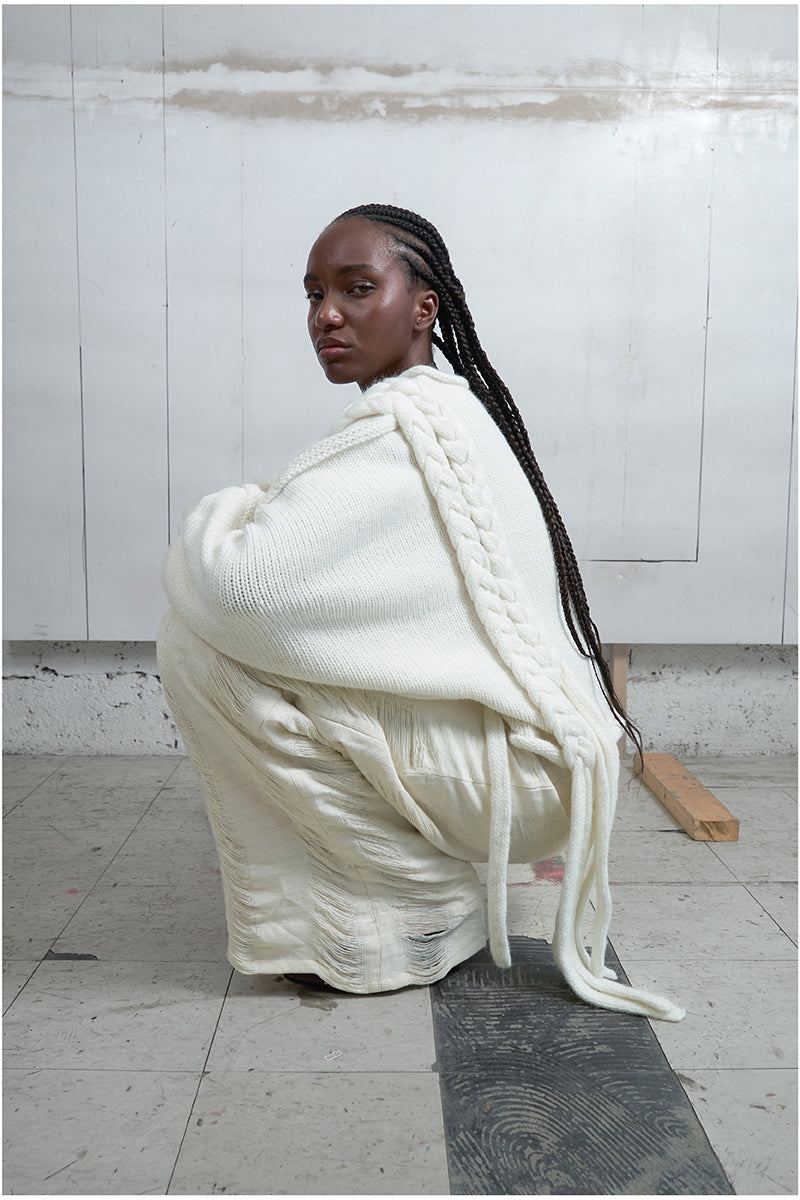 Ivory knitted sweater with long braids by MAZ Manuela Álvarez, featuring a cozy, textured design and long braided details.