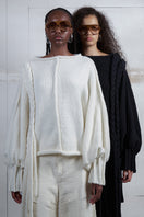 Ivory knitted sweater with long braids from MAZ Manuela Álvarez, featuring a cozy, textured knit design and long braided details.