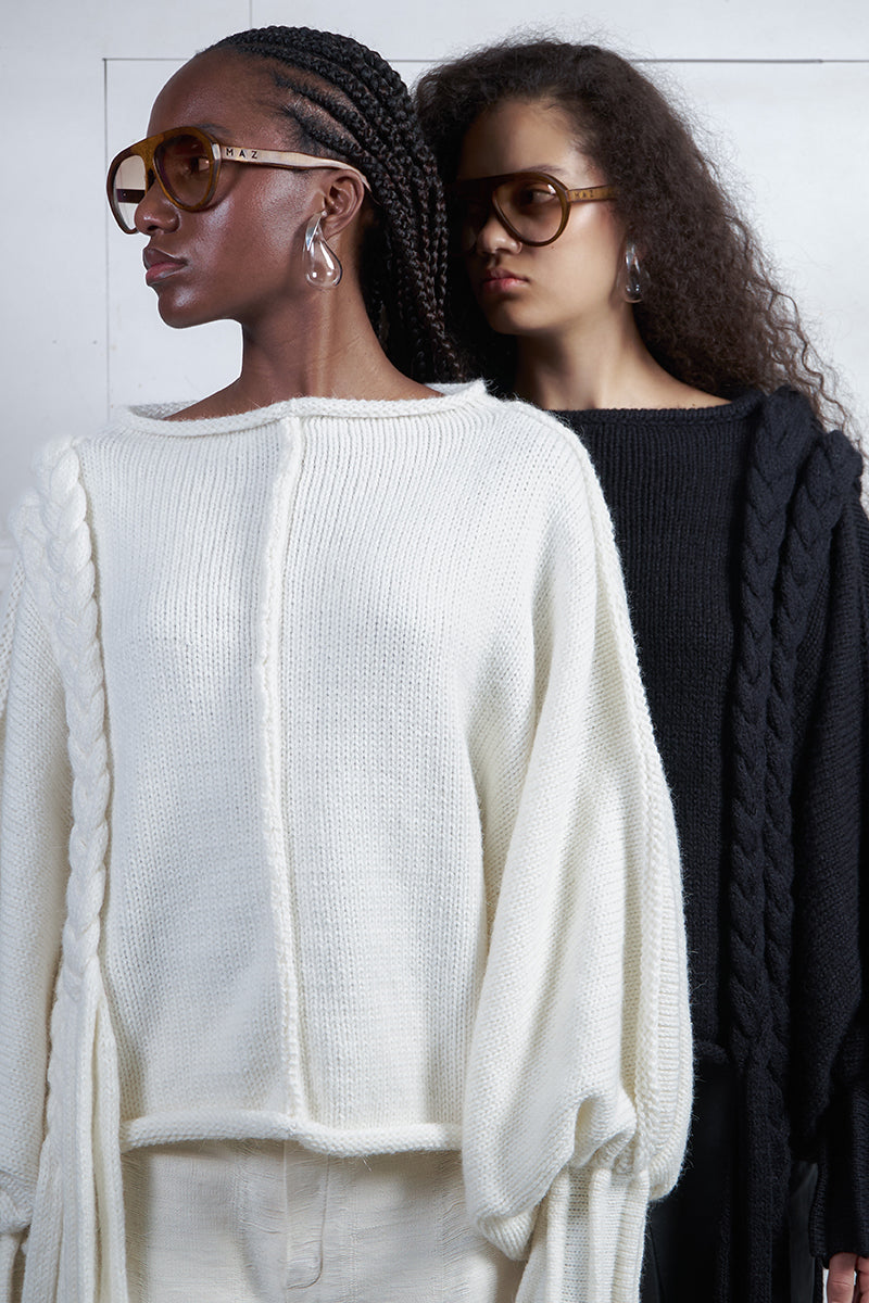 Ivory knitted sweater with long braids by MAZ Manuela Álvarez, showcasing cozy, textured knitwear with detailed braided design.