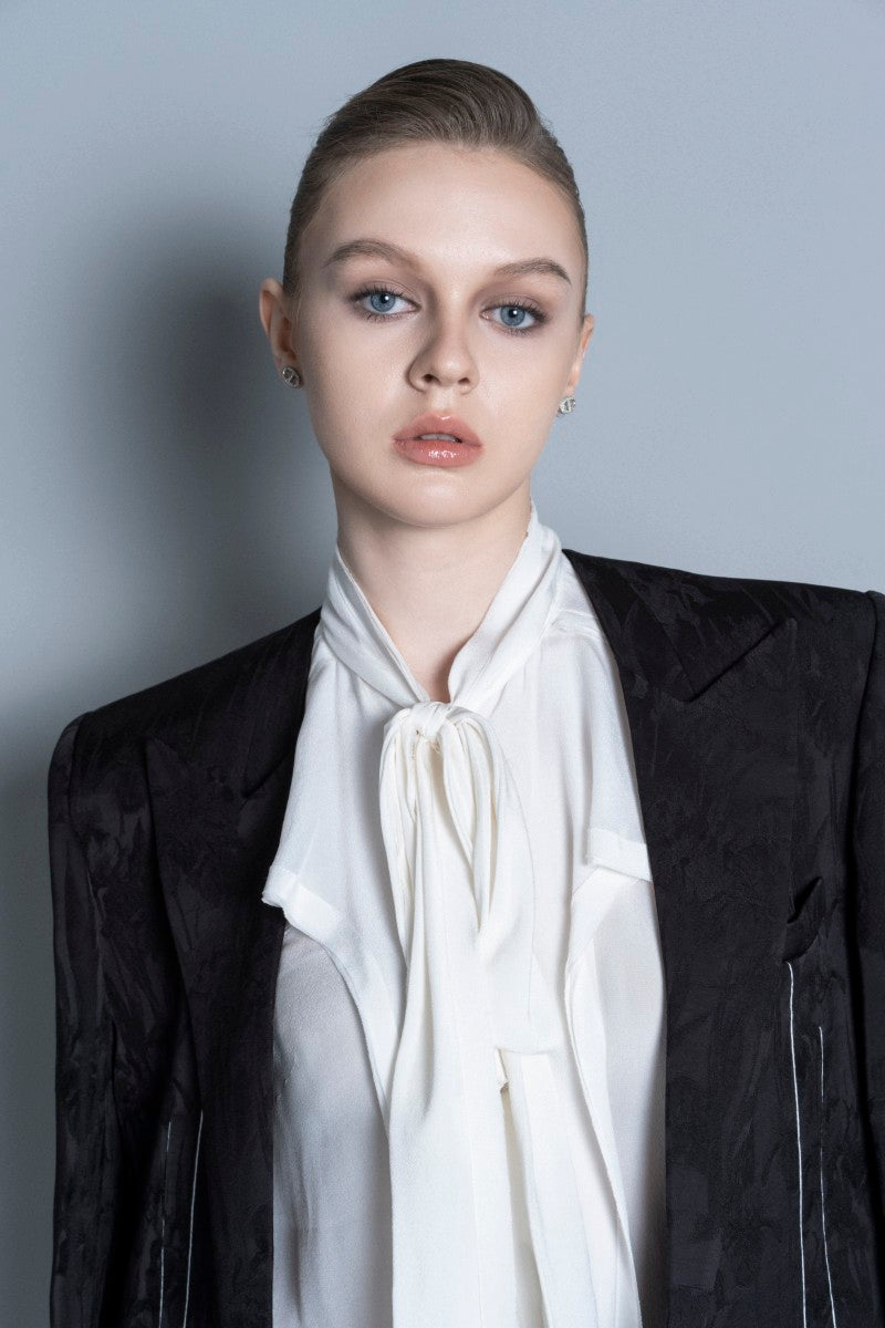 Black LEKIEU Grenoble jacket with a sleek design, shown hanging on a wooden hanger on a white background.