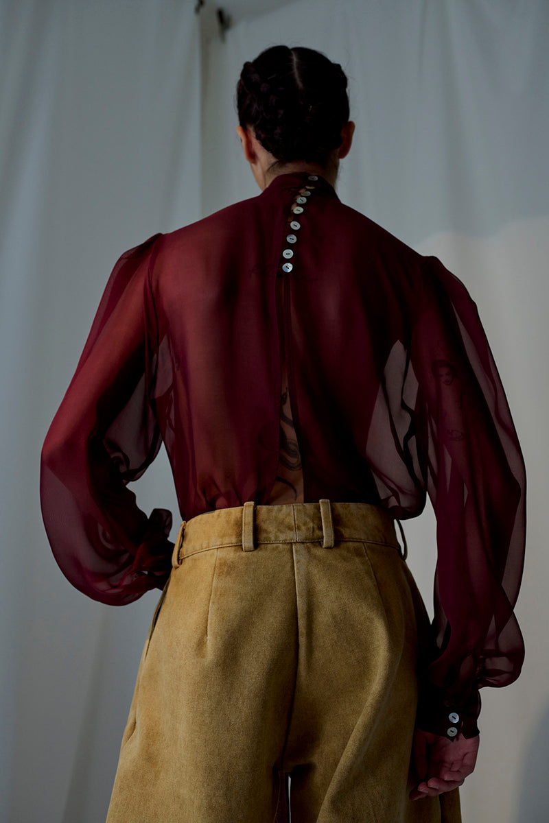 Brown Lorena Saravia Alex pants with a tailored fit, shown hanging on a wooden hanger.