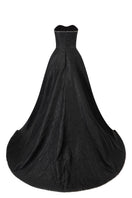 Black strapless floor-sweeping mullet overskirt gown by L'SCARLETT, shown from the back with flowing, layered fabric.