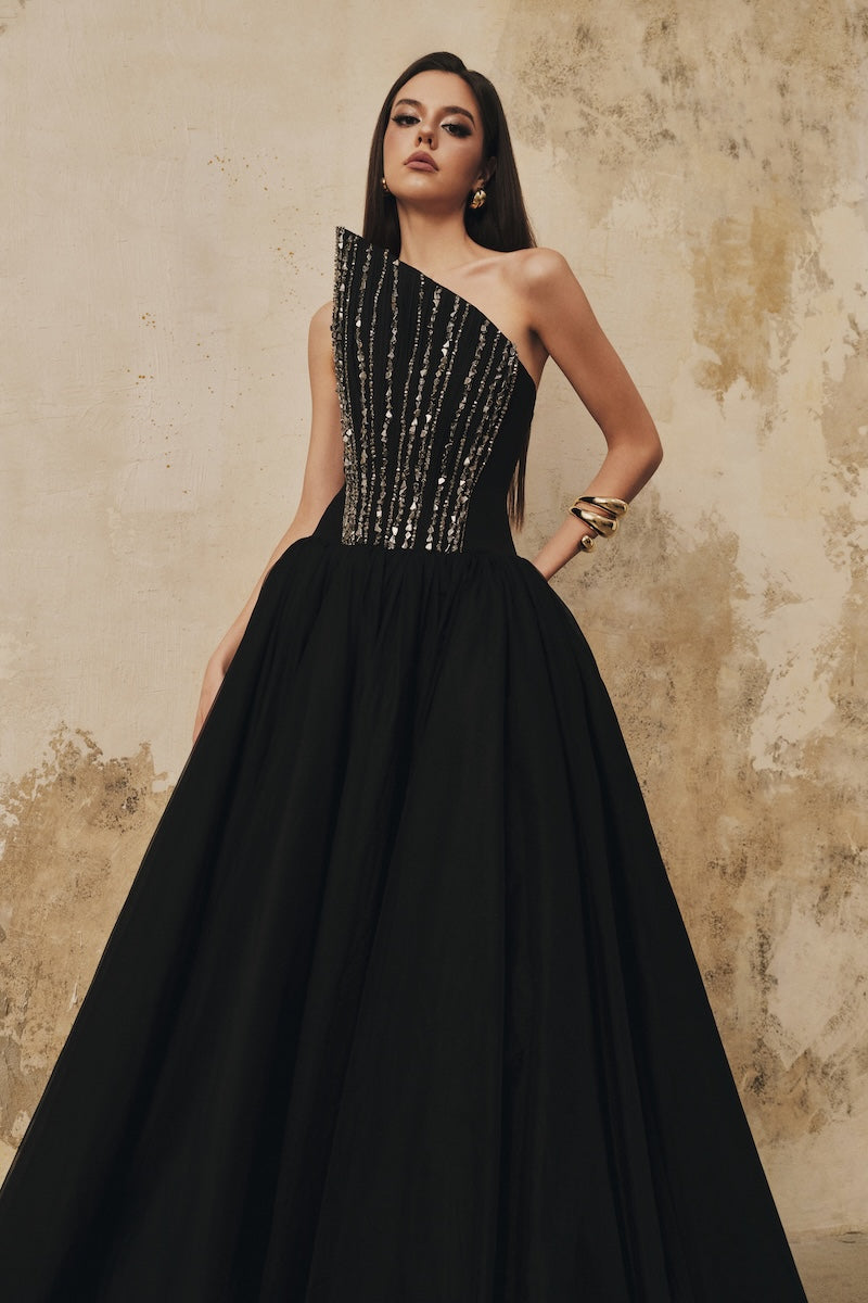 Black flared evening gown by L'SCARLETT featuring a pointed bustline, front draping, and crystal beading, maxi dress style.