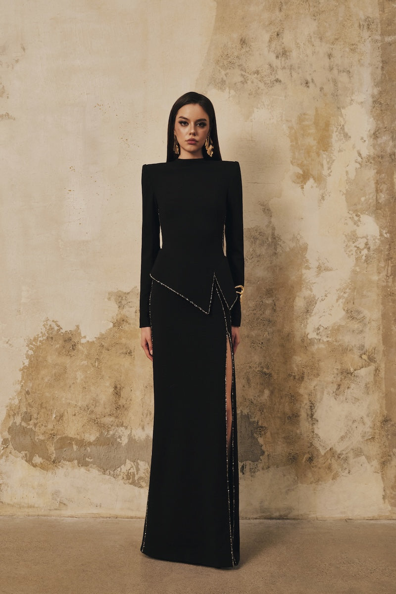 Black L'SCARLETT peplum high-neck maxi dress with long sleeves, front slit, and crystal beading details.