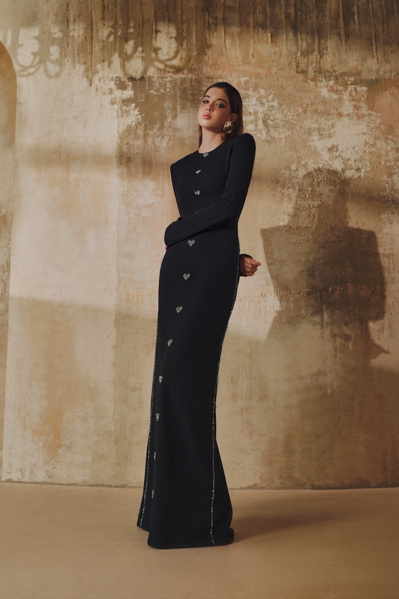 Black L'SCARLETT maxi dress with straight cut, long sleeves, and hand-embellished crystal heart details.