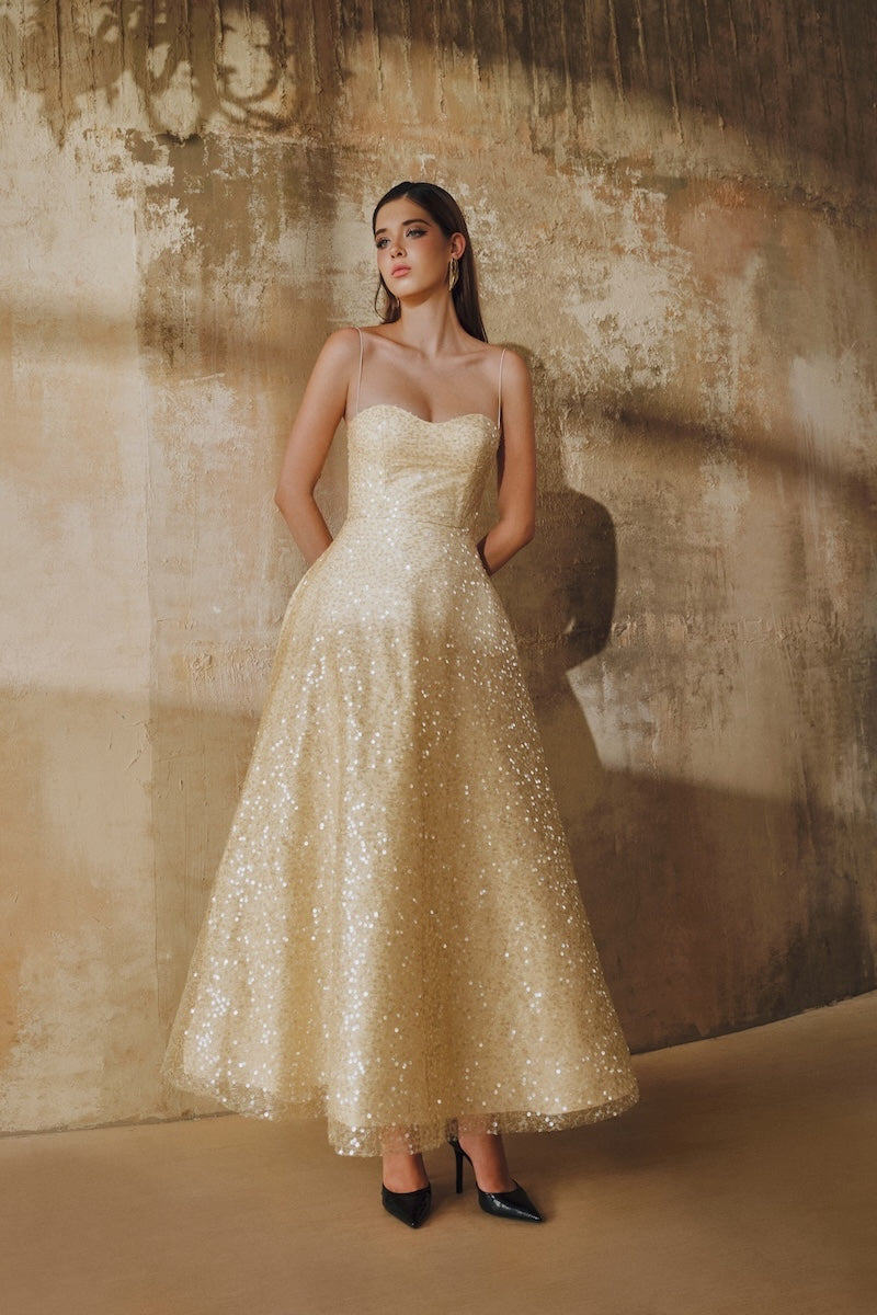 Light gold flared spaghetti-strap sequin midi dress by L'SCARLETT, showing its shimmering fabric and elegant fit.