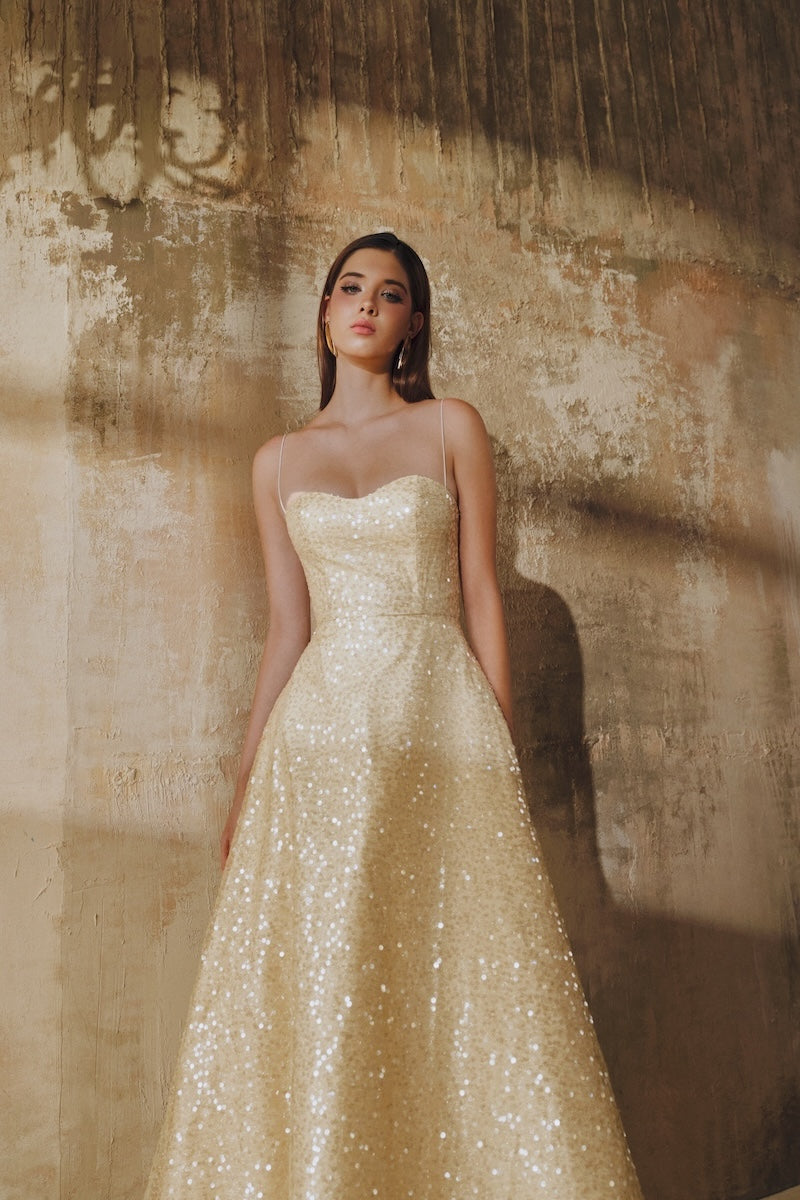 Light gold L'SCARLETT flared spaghetti-strap sequin midi dress displayed on a hanger, showcasing its elegant design and shimmering fabric.