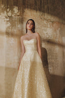 Light gold flared spaghetti-strap sequin gown by L'SCARLETT featuring a flowing silhouette and shimmering embellishments.