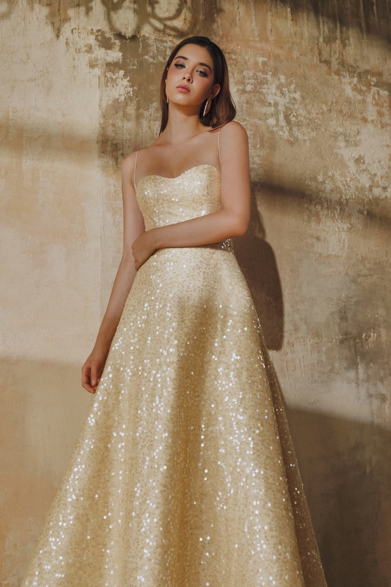 Light gold flared spaghetti-strap sequin midi dress by L'SCARLETT, shown on a model with a fitted bodice and flowing skirt.