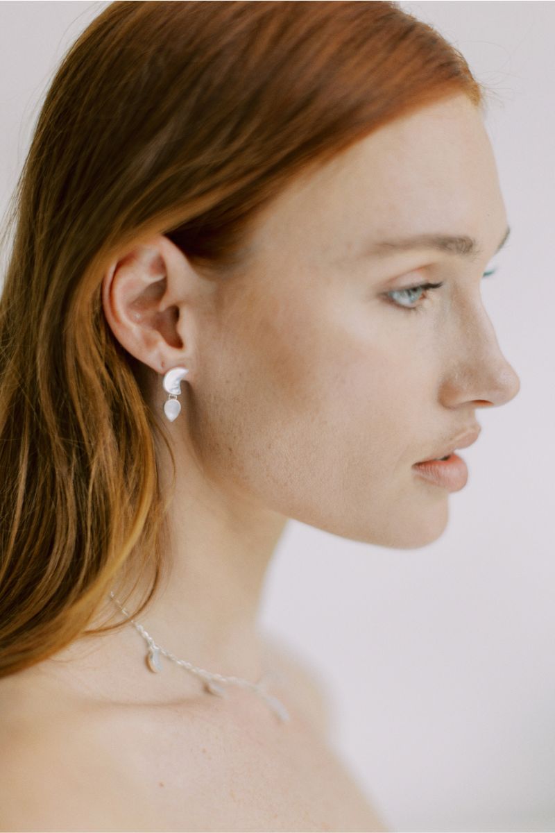 Silver petite moon earrings by Freya Rose, featuring a delicate moon design, worn as stylish jewelry in a lifestyle setting.