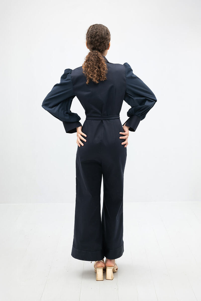 Navy blue Lilianne jumpsuit by ANA + MARIA, featuring a fitted silhouette and stylish neckline, displayed on a hanger.