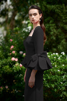 Black column gown by I.H.F with trapeze neckline and rose-draped three-quarter sleeves, elegant and form-fitting.
