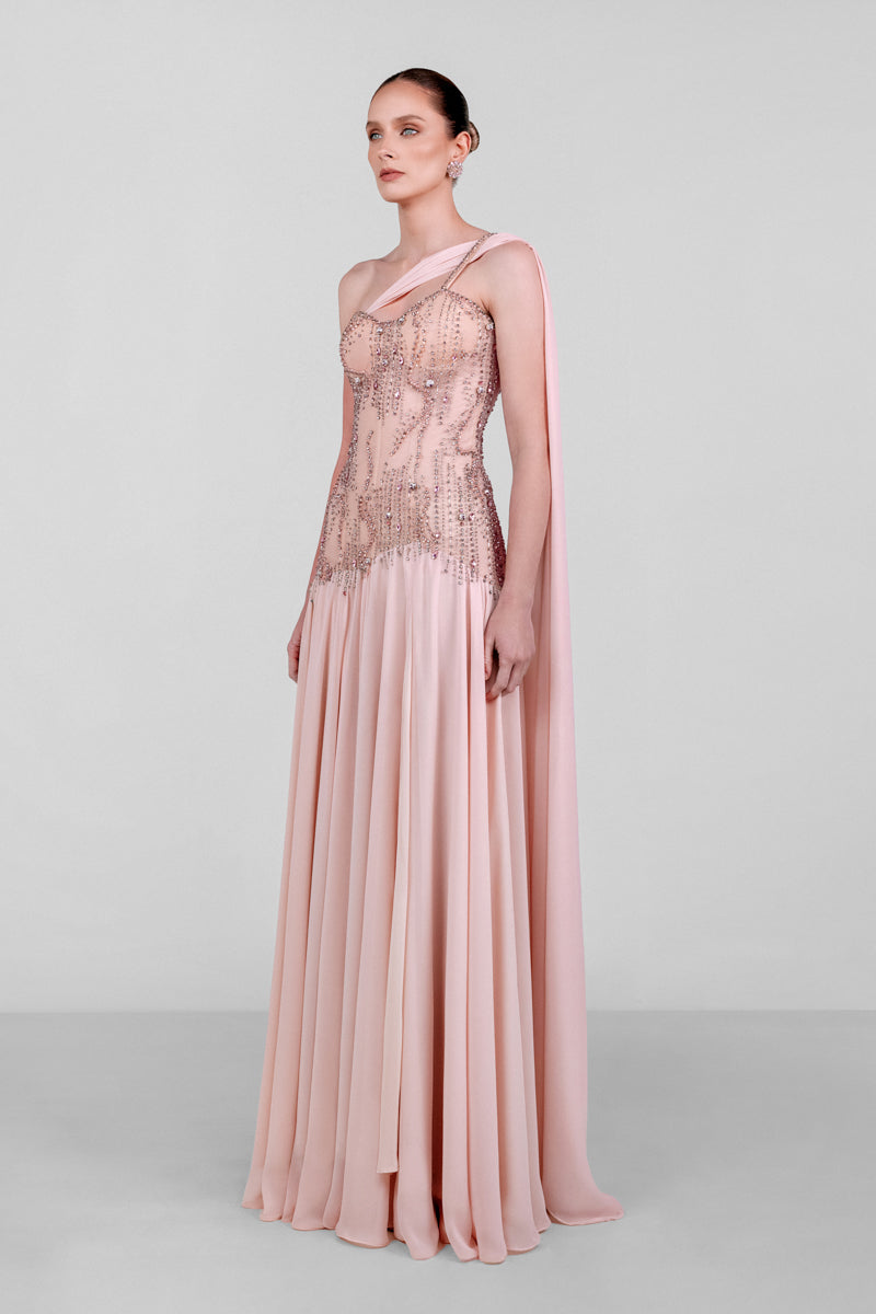 Elegant blush embellished cape gown by Monika Dimova featuring intricate detailing and flowing fabric for formal occasions.