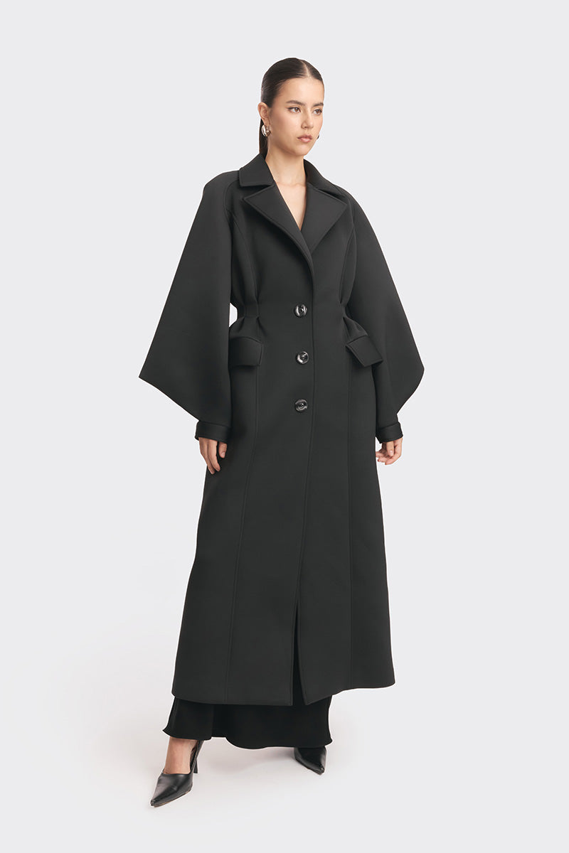 Black MS. Doll coat by Stolen Stores displayed on a hanger, showcasing the stylish design and fabric details.