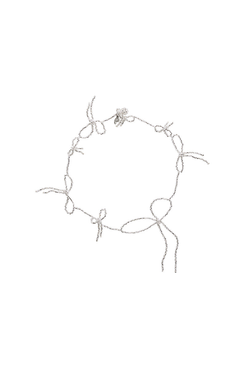 Silver multi-bow necklace by Pura Utz featuring layered bow design and delicate chain on a neutral background.