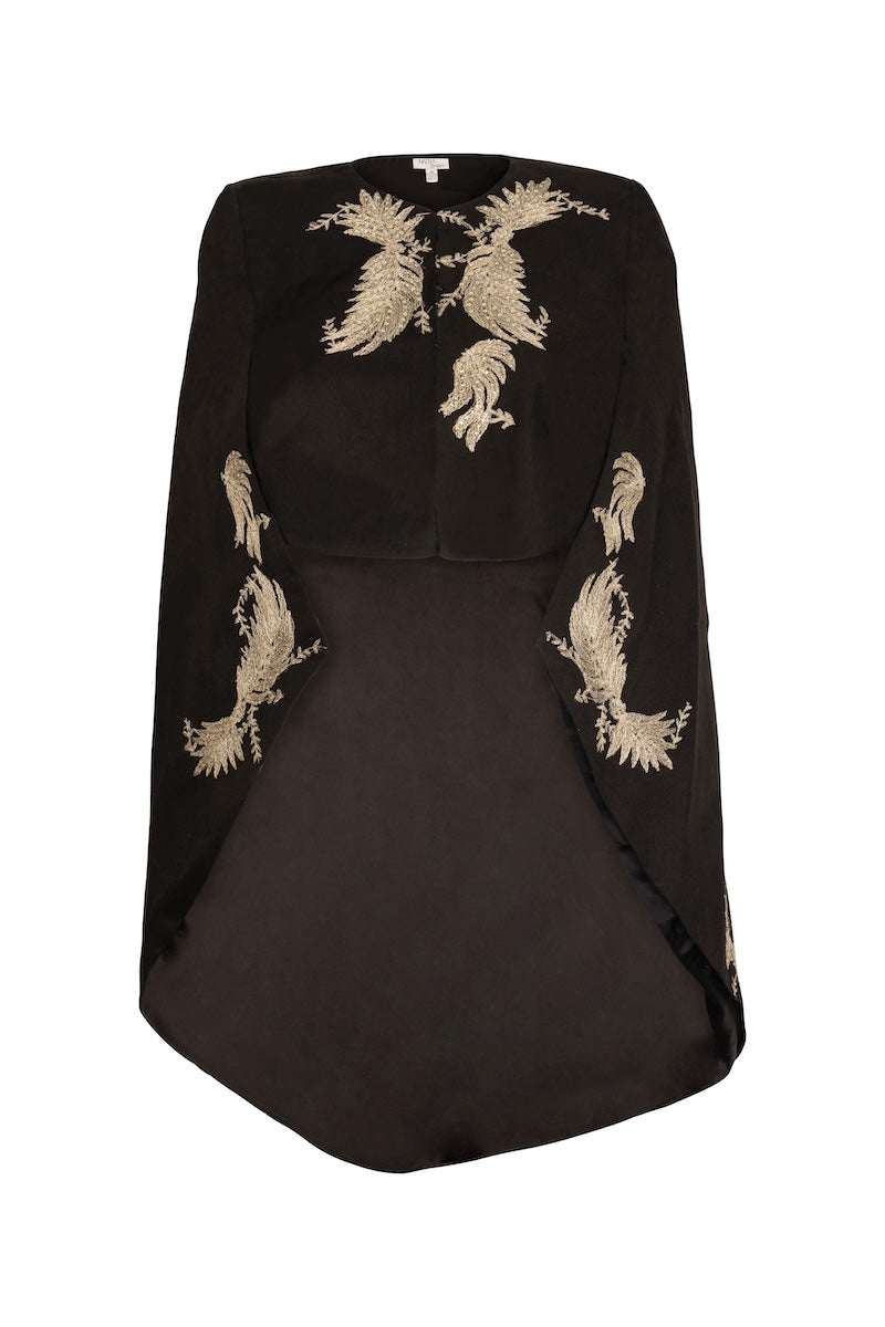 Nadya Shah Phoebe Cape jacket shown hanging on a wooden wall, featuring a stylish, draped design in neutral fabric.