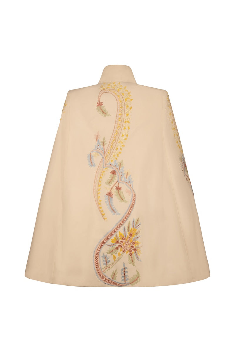 Ivory Dorian cape by Nadya Shah, stylish jacket with elegant draping and detailed design, displayed on a hanger.