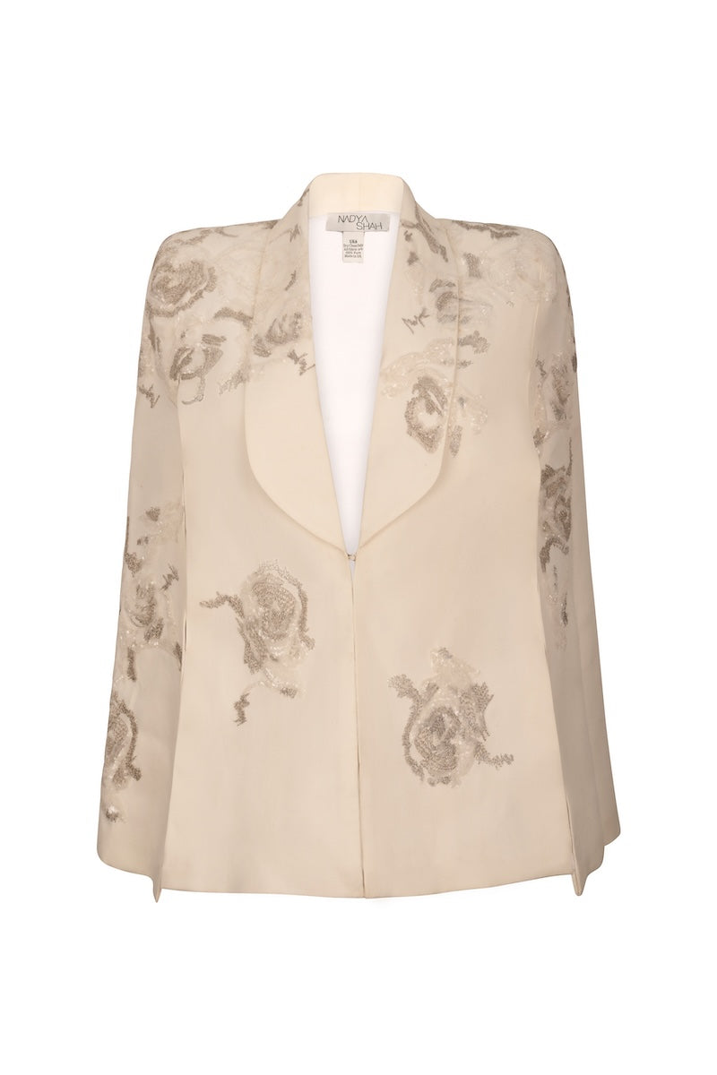 Nadya Shah Lumiere Cape jacket featuring elegant fabric and stylish design, displayed on a hanger with a neutral background.