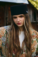 Black pillbox hat by LE SH KA, close-up of the sleek, structured hat with a smooth finish and classic silhouette.