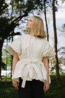 ANA + MARIA Nonora ivory blouse, stylish women’s top with a soft fabric and elegant design, shown in a campaign photo.