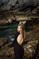 Black OLYA maxi dress by Suncillo displayed on a hanger with flowing fabric and elegant design.