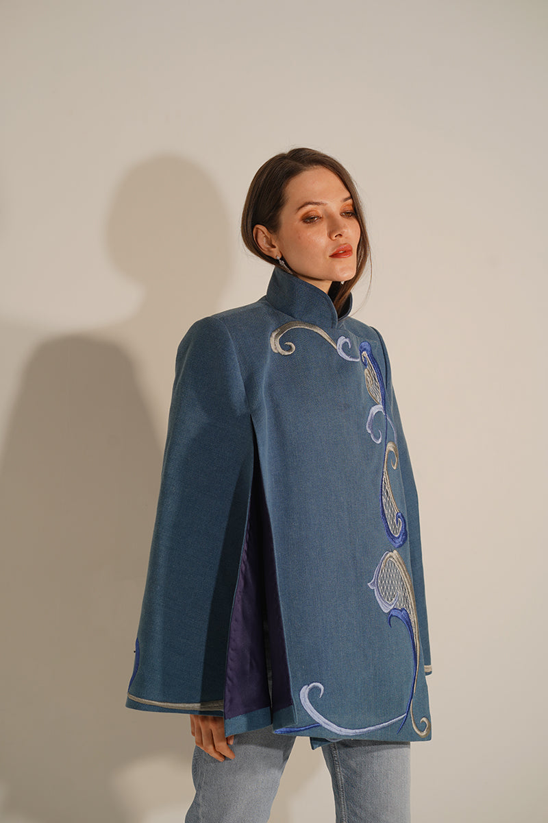 Nadya Shah Olympia denim cape jacket with classic blue denim fabric and stylish design, displayed on a hanger.