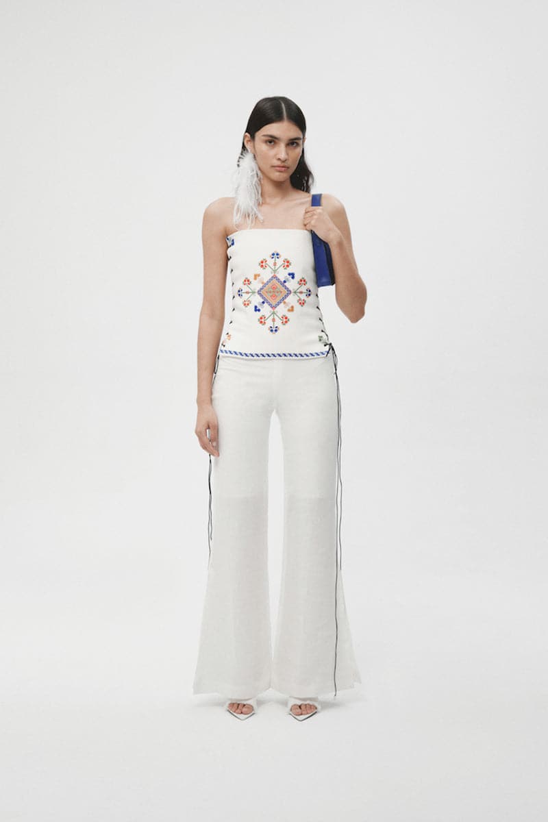 White organic linen flared pants from JC Pajares, shown hanging with a relaxed fit and wide leg design.