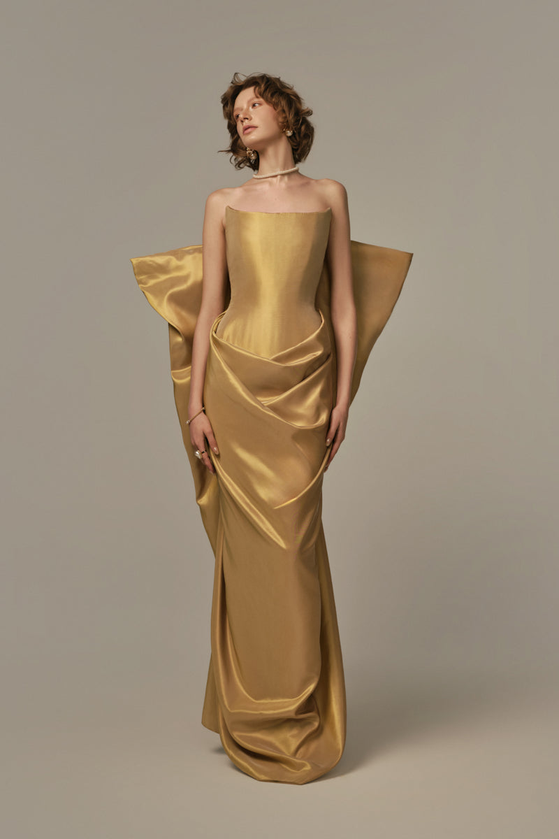 Elegant gold Palais gown by POEM featuring intricate details and flowing fabric, displayed on a model.
