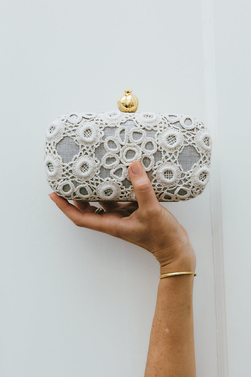 Silver clutch purse by Sarah's Bag featuring a crocheted pomegranate design on a sleek silver box.
