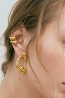 Gold earrings by Eugenia Ospina featuring intricate design, showcased on a neutral background.
