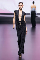 Black deep plunge maxi gown by CEM featuring a elegant brooch detail and flowing fabric.
