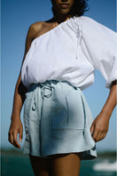 White Ana + Maria Rohe cropped top displayed on a hanger, showcasing its stylish, fitted design and lightweight fabric.