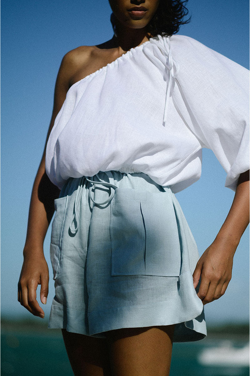 White Ana + Maria Rohe cropped top displayed on a hanger, showcasing its stylish, fitted design and lightweight fabric.