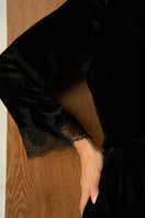 Black velvet lace robe from MANITO, featuring elegant lace details and a flowing design, shown hanging on a wooden hook.