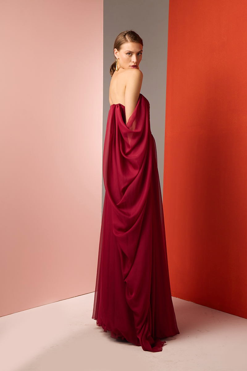 Red strapless gown by Joanna Andraos, featuring elegant design and flowing fabric, shown from a side view.