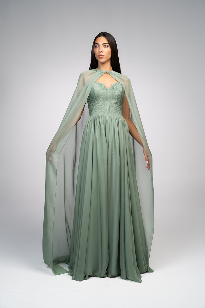 Elegant strapless gown by Joanna Andraos with a detachable cape, featuring flowing fabric and sophisticated design.
