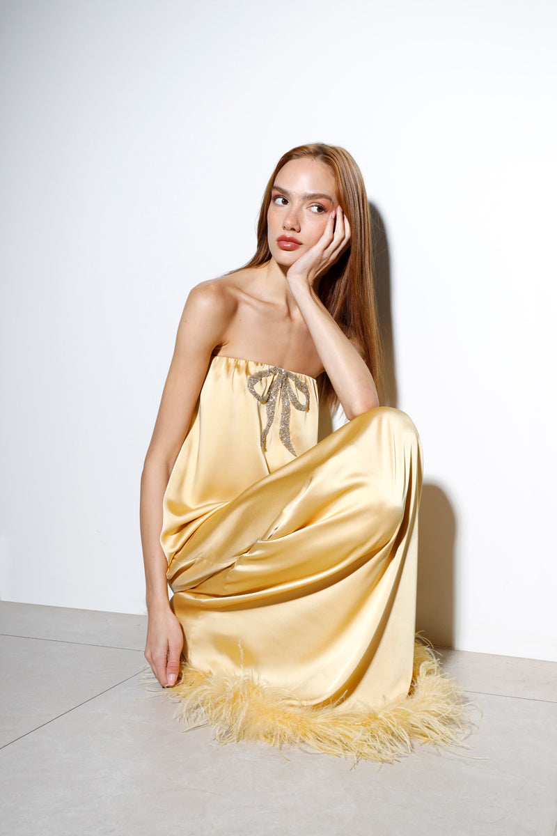 Butter yellow satin gown with a bow detail, designed by Rayane Bacha, featuring elegant flowing fabric and a sophisticated look.
