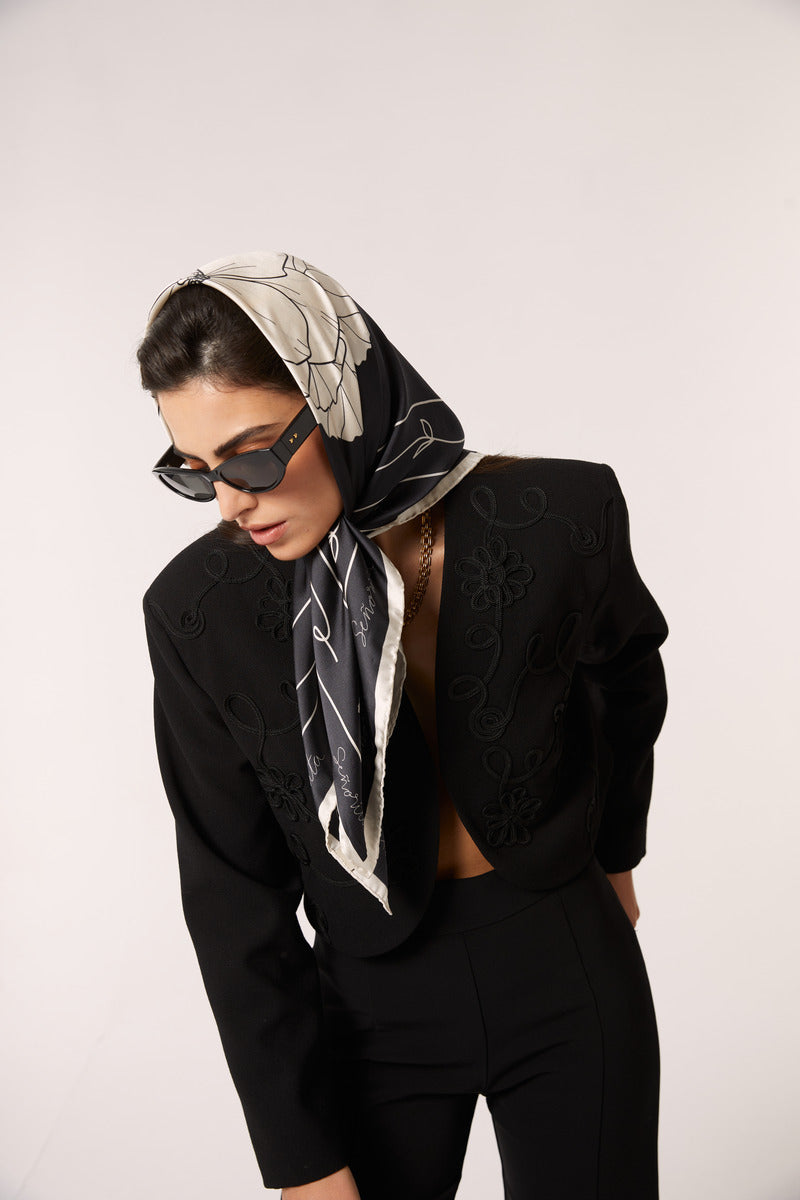 Black Señorita Luisa scarf draped over a neutral background, showcasing soft fabric and stylish, versatile design.