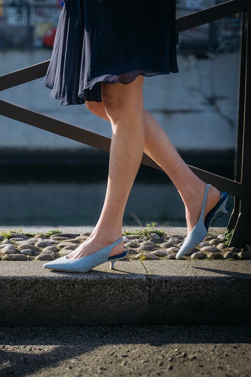A pair of AERA Silvana blue denim slingback heel pumps with pointed toes and ankle straps on a neutral background.